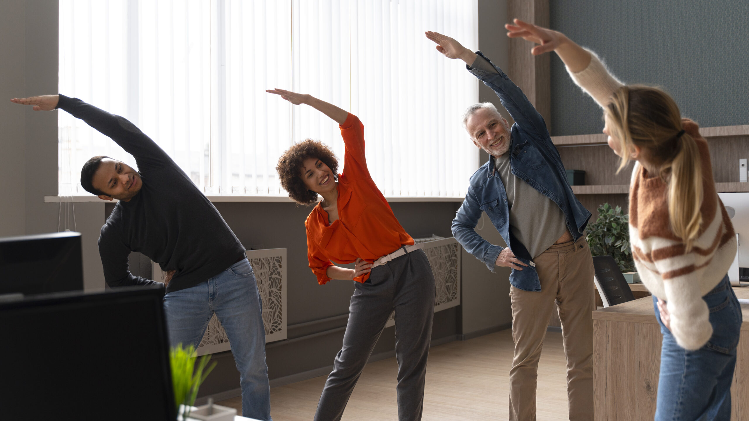 Colaboradores praticando ginástica laboral no ambiente de trabalho, realizando alongamentos em suas estações para promover saúde e bem-estar.