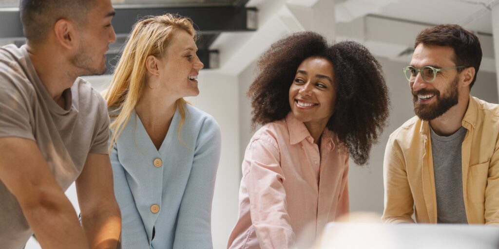 Equipe diversa de profissionais sorrindo em um espaço corporativo, demonstrando um ambiente de trabalho saudável e acolhedor.