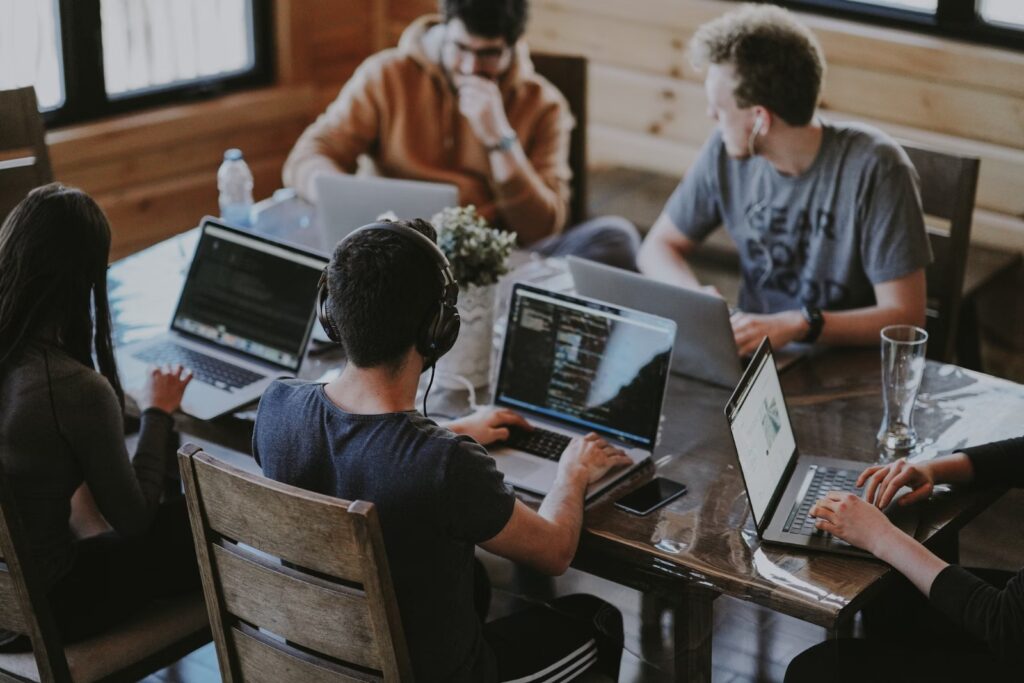 Grupo de jovens profissionais trabalhando em equipe e compartilhando ideias em um ambiente colaborativo, todos utilizando notebooks para estratégias de benefícios corporativos.
