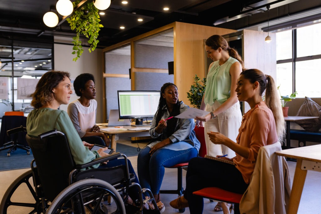 Profissional sorrindo em cadeira de rodas durante reunião em escritório moderno de startup, representando inclusão e cultura de benefícios flexíveis no ambiente de trabalho.