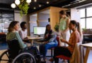 Profissional sorrindo em cadeira de rodas durante reuni&atilde;o em escrit&oacute;rio moderno de startup, representando inclus&atilde;o e cultura de benef&iacute;cios flex&iacute;veis no ambiente de trabalho.