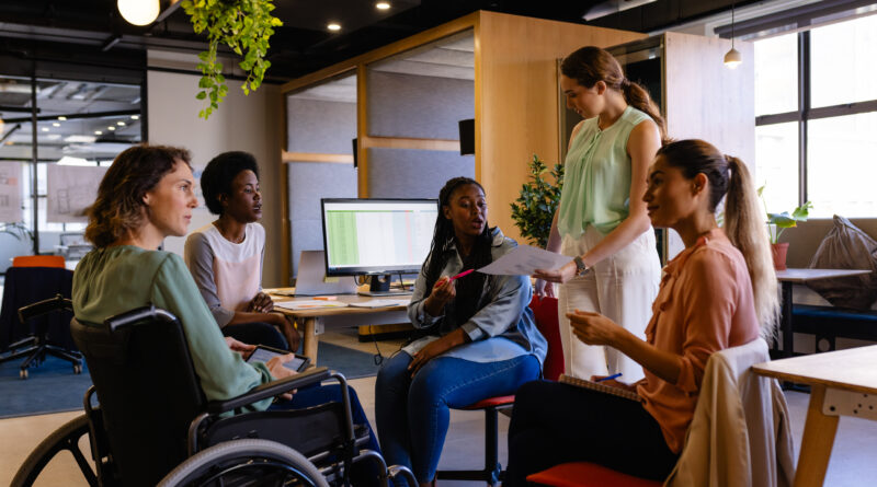 Profissional sorrindo em cadeira de rodas durante reunião em escritório moderno de startup, representando inclusão e cultura de benefícios flexíveis no ambiente de trabalho.