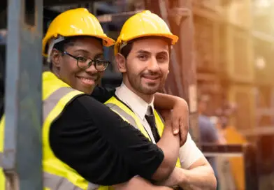 Riscos Psicossociais NR-1: trabalhadores da ind&uacute;stria usando capacete e colete de seguran&ccedil;a em ambiente operacional, representando bem-estar, colabora&ccedil;&atilde;o e cuidado no trabalho.