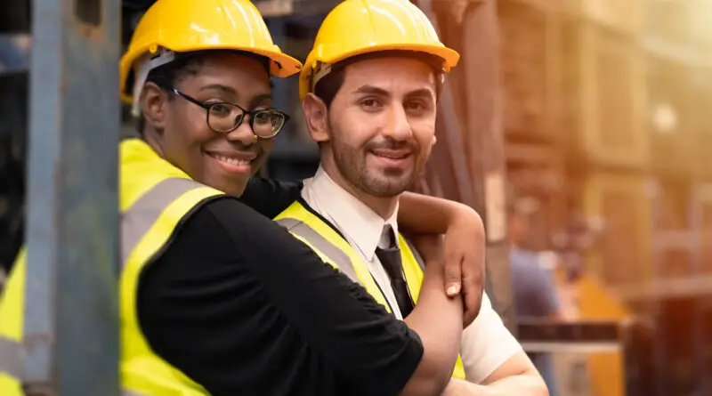 Riscos Psicossociais NR-1: trabalhadores da ind&uacute;stria usando capacete e colete de seguran&ccedil;a em ambiente operacional, representando bem-estar, colabora&ccedil;&atilde;o e cuidado no trabalho.