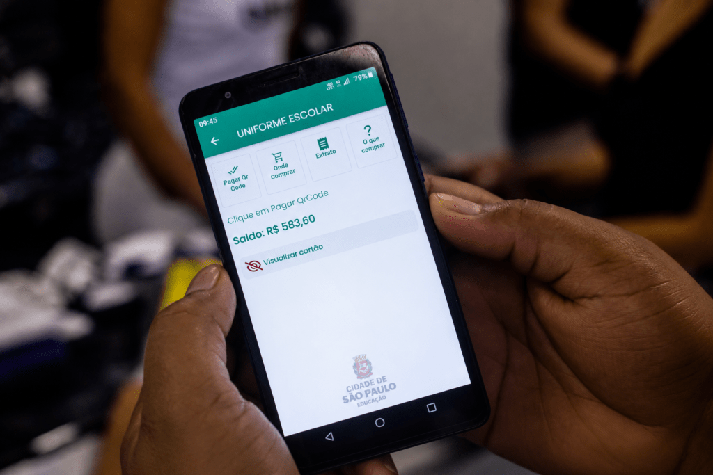 Pessoa utiliza aplicativo de uniforme escolar no celular, exemplo de crédito digital aplicado à gestão de benefícios sociais.