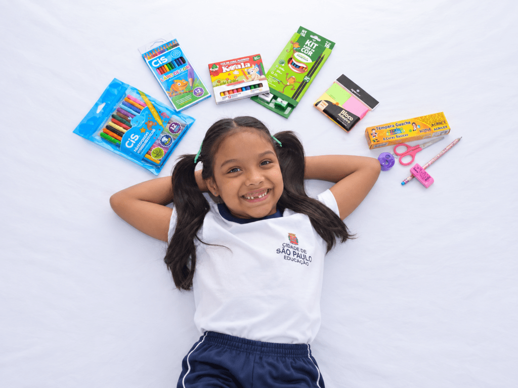 Menina com uniforme escolar cercada por materiais escolares, representando a gestão de benefícios sociais por meio de programas públicos.